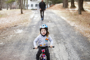Boy riding bicycle on road with father in background - CAVF07874