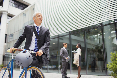 Businessman walking bicycle outside of office building stock photo