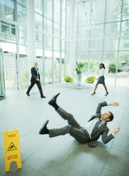 Geschäftsmann rutscht auf dem Boden eines Bürogebäudes aus - CAIF15785