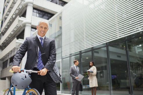 Businessman walking bicycle outside of office building - CAIF15796