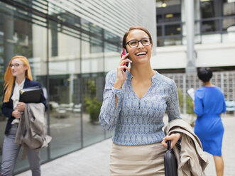 Geschäftsfrau, die außerhalb eines Bürogebäudes mit einem Handy telefoniert - CAIF15800