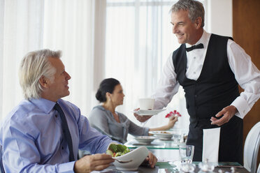 Kellner serviert einem reifen Mann am Tisch im Restaurant eine Tasse Kaffee - CAIF15837