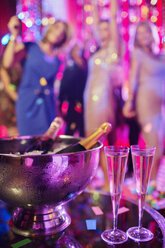 Champagnerflaschen in Eiskübeln und Champagnerflöten in einem Nachtclub, tanzende Menschen im Hintergrund - CAIF15838