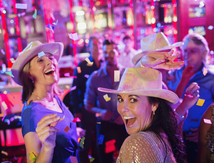 Confetti falling on women wearing cowboy hats laughing and dancing in nightclub - CAIF15849