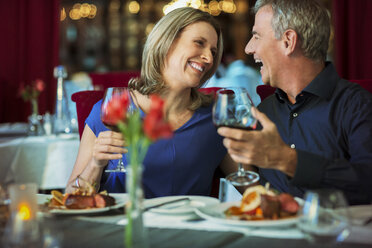 Lächelndes glückliches reifes Paar, das sich ansieht und Gläser mit Rotwein in einem Restaurant hält - CAIF15851