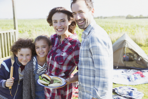 Porträt einer lächelnden Familie mit gegrillten Hamburgern auf einem sonnigen Campingplatz, lizenzfreies Stockfoto