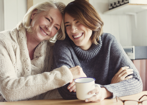 Laughing mother and daughter in sweaters hugging and drinking coffee stock photo
