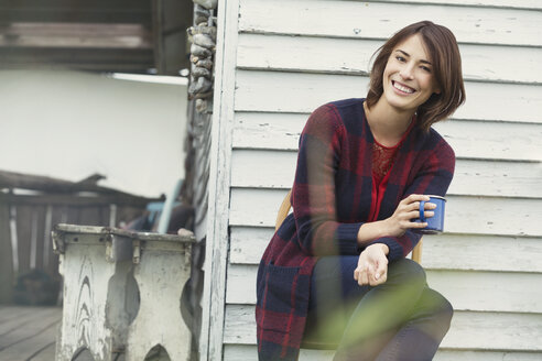 Portrait smiling brunette woman drinking coffee on porch - CAIF15894