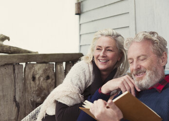 Lächelndes älteres Paar, das auf der Terrasse ein Buch liest - CAIF15904