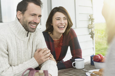 Smiling couple talking at table on patio - CAIF15905