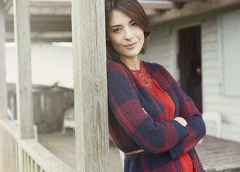 Portrait smiling brunette woman in sweater on porch - CAIF15914