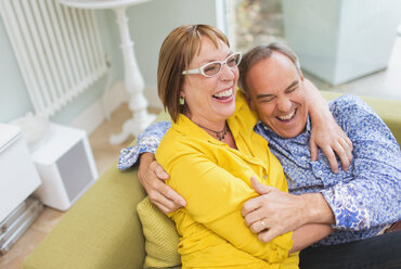 Älteres Paar lachend und umarmend auf dem Sofa - CAIF15920