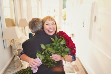 Glückliche Frauen, die einen Rosenstrauß erhalten und ihren Mann umarmen - CAIF15921