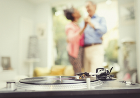 Älteres Paar tanzt im Wohnzimmer hinter dem Plattenspieler, lizenzfreies Stockfoto