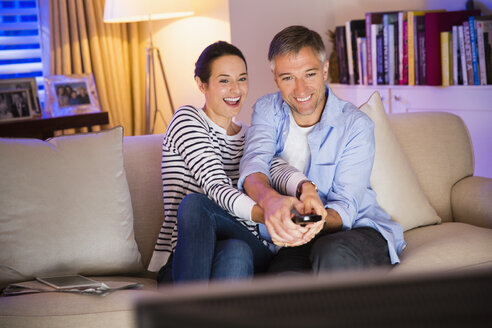 Verspieltes Paar kämpft um die Fernbedienung beim Fernsehen im Wohnzimmer - CAIF15945