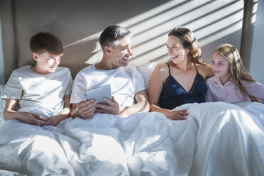 Smiling family laying in bed using digital tablet - CAIF15948