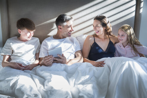 Lächelnde Familie, die im Bett liegt und ein digitales Tablet benutzt - CAIF15948
