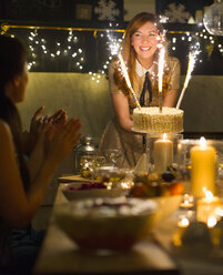 Enthusiastische Frau serviert Kuchen mit Wunderkerzen-Feuerwerk an klatschende Freunde - CAIF15979