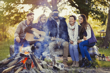 Lächelnde Freunde mit Fotohandy machen ein Selfie am Lagerfeuer - CAIF15986