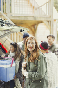 Porträt einer lächelnden Frau mit Freunden, die eine Kühlbox aus einem Auto ausladen - CAIF15988