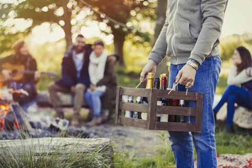 Man carrying crate of wine and beer at campsite with friends - CAIF15989