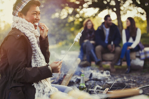 Smiling woman eating roasted marshmallows at campfire - CAIF15997