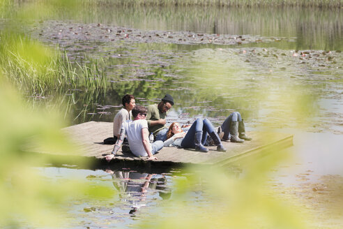 Friends laying and relaxing on sunny dock at lakeside - CAIF16000