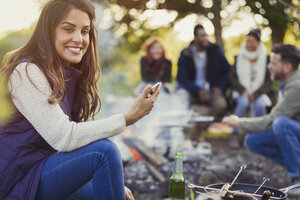 Porträt einer lächelnden Frau, die auf einem Campingplatz eine SMS schreibt und Bier trinkt - CAIF16012