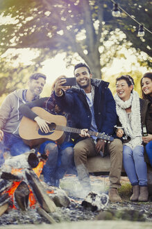 Freunde mit Gitarre machen Selfie mit Fotohandy am Lagerfeuer - CAIF16013