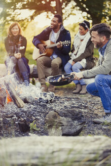 Friends playing guitar and cooking hot dogs at campfire - CAIF16015