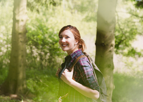 Lächelnde Frau mit Rucksack beim Wandern im sonnigen Wald, lizenzfreies Stockfoto