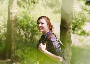 Lächelnde Frau mit Rucksack beim Wandern im sonnigen Wald - CAIF16016