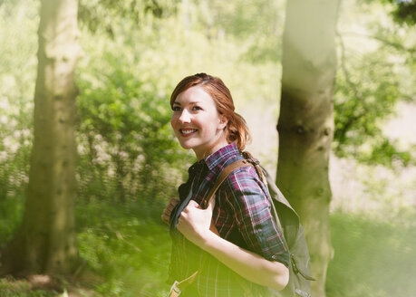Smiling woman with backpack hiking in sunny woods - CAIF16016