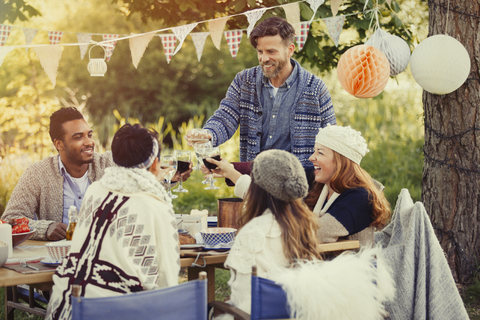 Freunde stoßen mit Weingläsern am Mittagstisch im Garten an, lizenzfreies Stockfoto