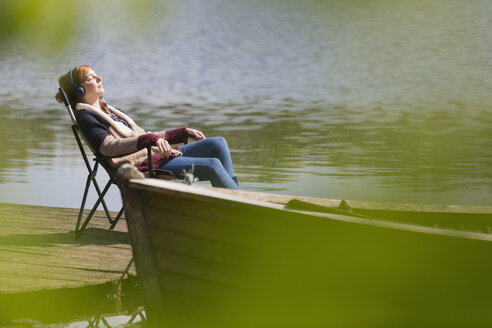 Serene woman relaxing listening to music with headphones at sunny lakeside dock - CAIF16020