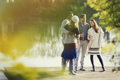 Couples talking drinking champagne on lakeside dock - CAIF16021