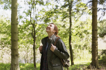 Lächelnde Frau beim Wandern mit Blick auf Bäume in einem sonnigen Wald - CAIF16036