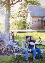 Paar nimmt Selfie mit Kamera-Handy am Lagerfeuer außerhalb Hütte - CAIF16047