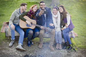 Freunde mit Gitarre nehmen Selfie mit Kamera-Handy auf dem Campingplatz - CAIF16048