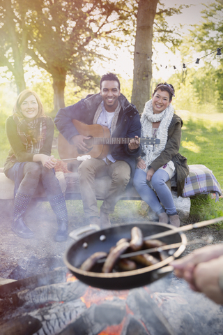 Freunde mit Gitarre kochen Hot Dogs über dem Lagerfeuer, lizenzfreies Stockfoto