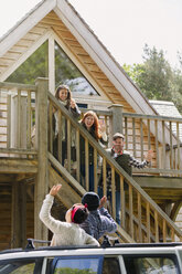 Friends on stairs waving to friends in car outside sunny cabin - CAIF16052