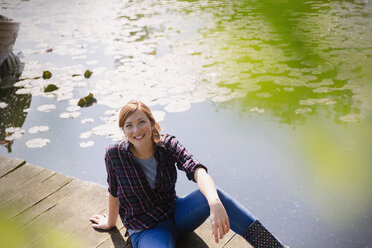 Porträt lächelnde Frau sitzt auf sonnigen Steg am See - CAIF16056
