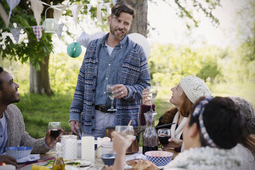 Mann stößt mit Freunden am Gartentisch an - CAIF16058