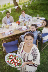 Porträt einer lächelnden Frau, die ihren Freunden am Tisch einer Gartenparty Caprese-Salat serviert - CAIF16059