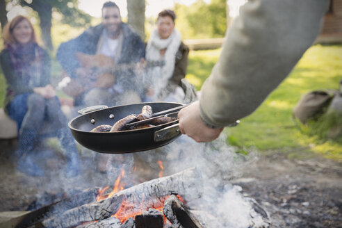 Mann kocht Hot Dogs über dem Lagerfeuer für Freunde - CAIF16069