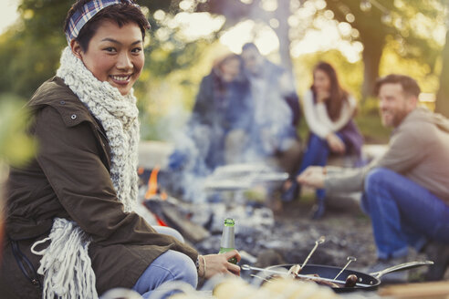 Portrait lächelnde Frau trinkt Bier mit Freunden am Lagerfeuer - CAIF16081