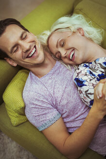 Zärtliches lachendes Paar auf dem Sofa mit geschlossenen Augen - CAIF16092