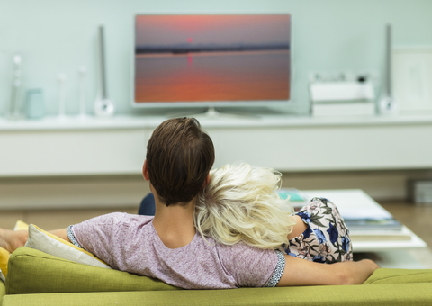 Entspanntes Paar beim Fernsehen auf dem Wohnzimmersofa, lizenzfreies Stockfoto