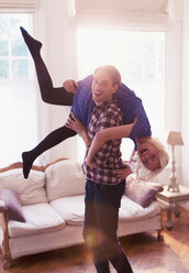 Portrait playful husband carrying wife over shoulder in living room - CAIF16096