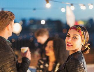 Porträt einer lächelnden jungen Frau auf einer nächtlichen Dachterrassenparty - CAIF16117